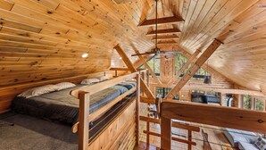 A wooden cabin with a loft bedroom, a bunk bed, and a view of the outdoors.