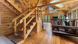 A wooden interior with a staircase, bookshelves, and large windows.