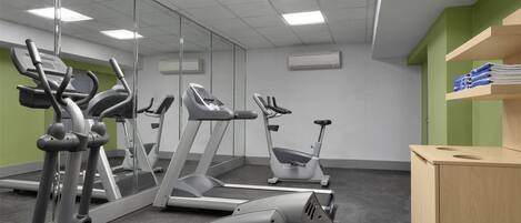 Une salle de sport équipée de machines de cardio, de miroirs et d’un meuble en bois contenant des serviettes.