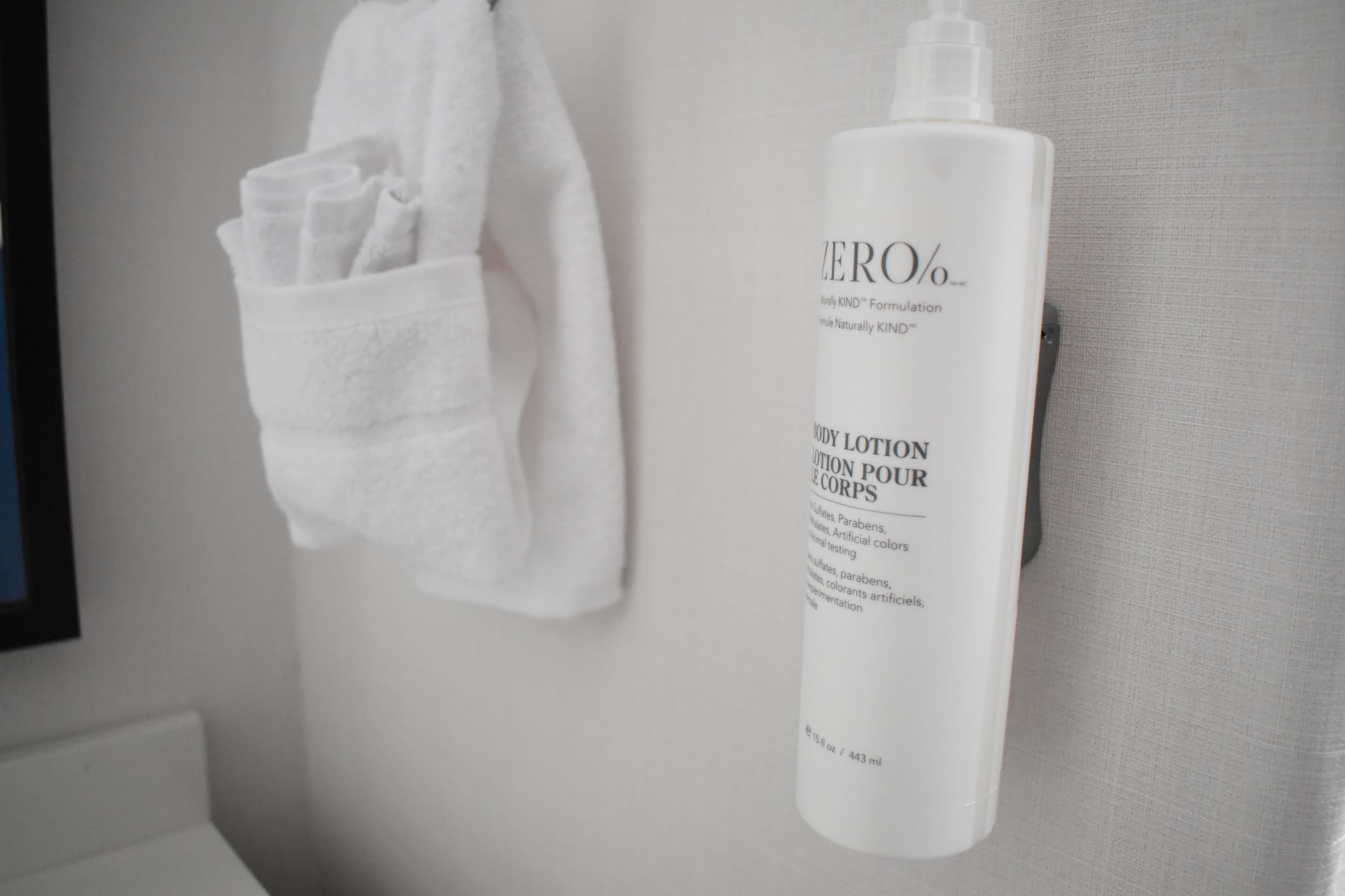 A bathroom with a white towel hanging on a towel rack and a bottle of Zero% body lotion on the wall.