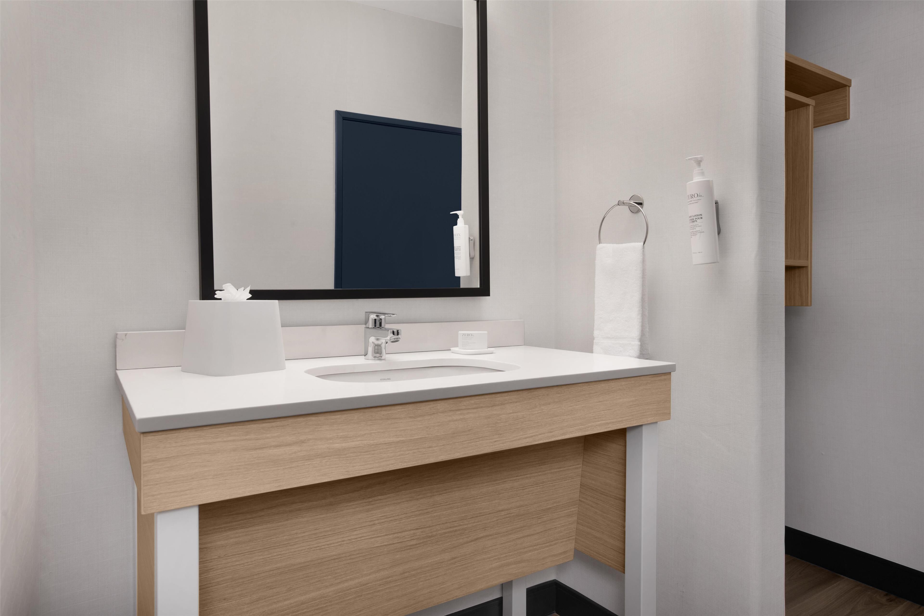 A modern bathroom with a white sink, wooden vanity, and a large mirror.