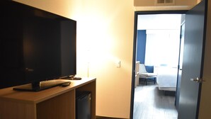 A hotel room with a TV on a wooden stand, a desk with a computer and a chair, and a bed with a blue headboard. - Spark By Hilton Albuquerque North I-25 (Albuquerque)