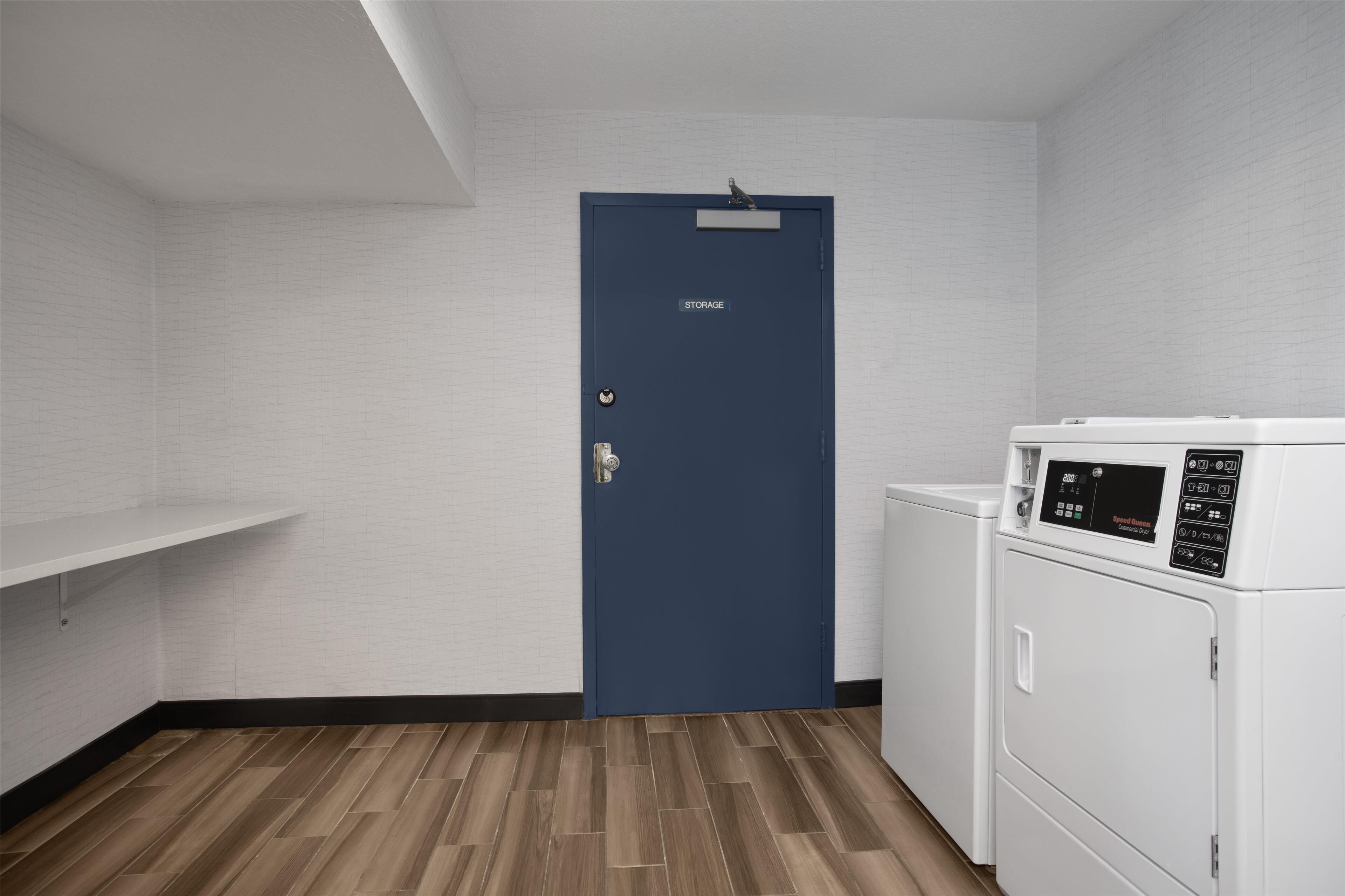 Une buanderie avec une porte bleue portant l’inscription « RANGEMENT », un lave-linge blanc et un plancher en bois.