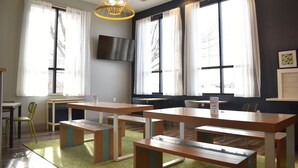 A modern classroom with wooden tables and benches, large windows with white curtains, and a flat-screen TV mounted on the wall. - Spark By Hilton Albuquerque North I-25 (Albuquerque)