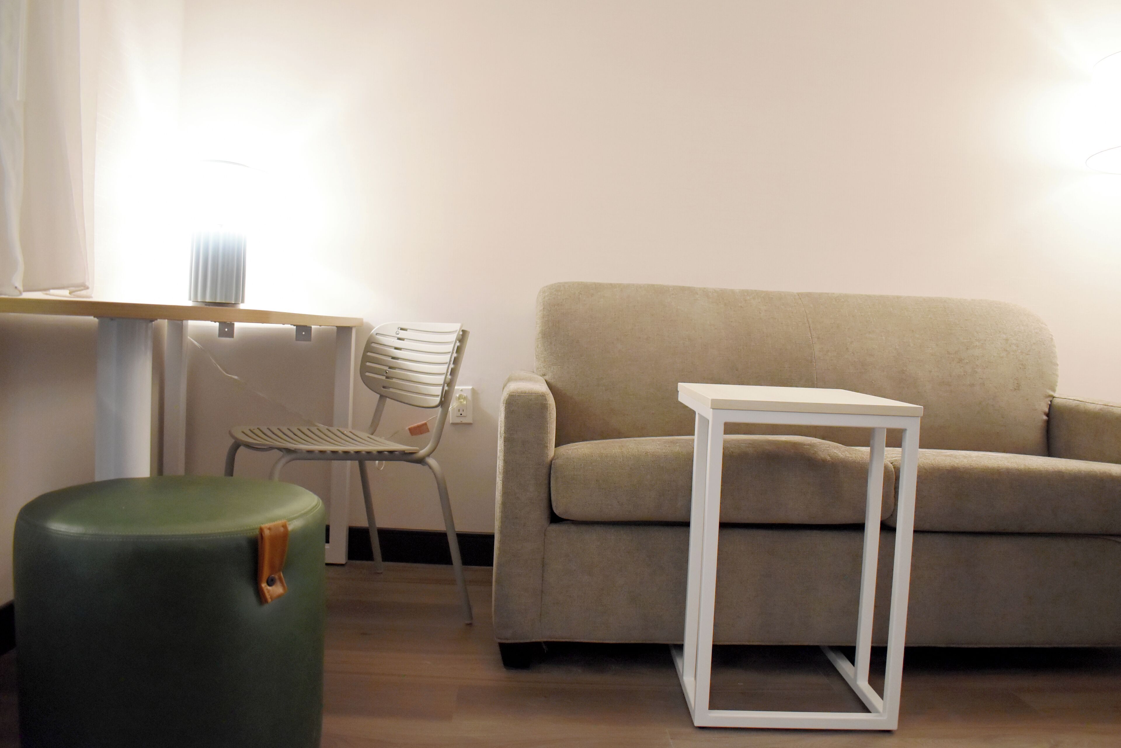 Een woonkamer met een groene poef, een witte tafel, een beige bank en een stoel.