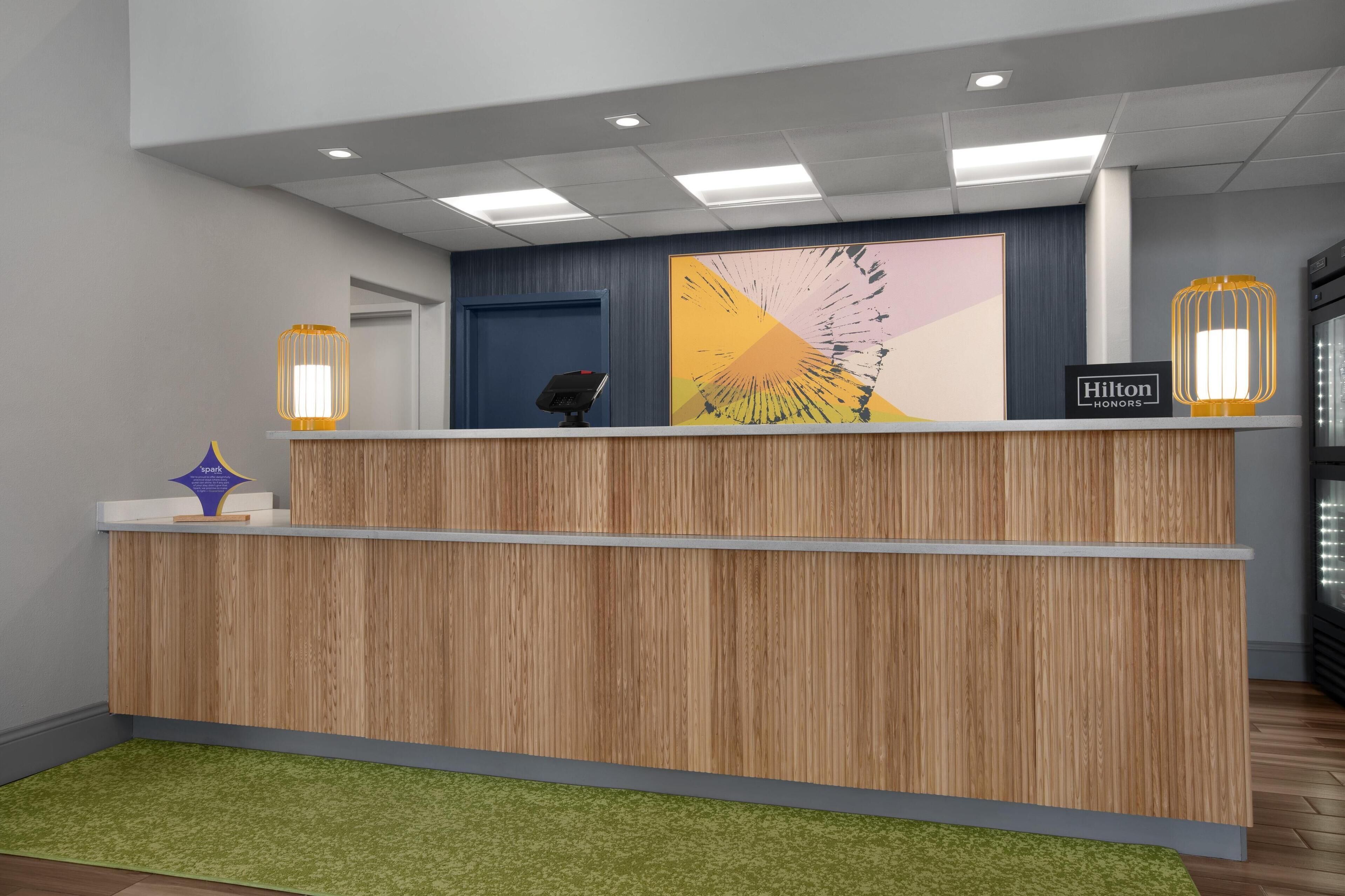 A modern reception desk with a wooden finish, a digital display, and two wall-mounted lamps.