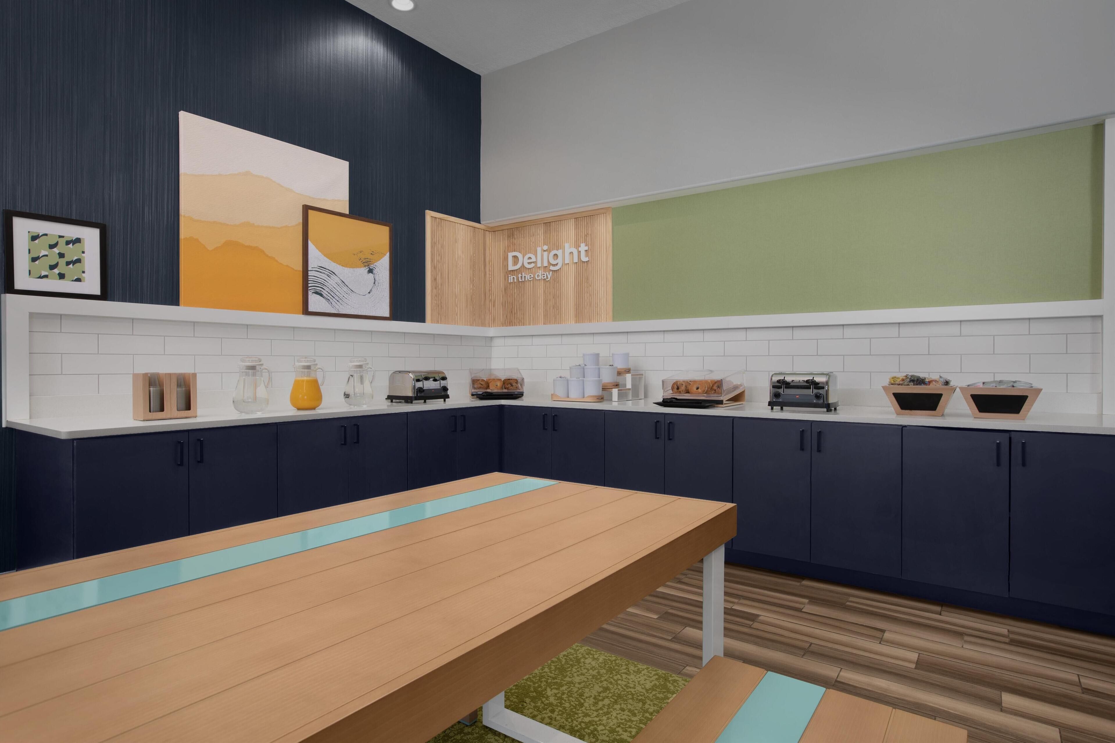 Een moderne keuken met donkerblauwe kastjes, een houten tafel en een bordje met de tekst 'Geniet van de dag'.