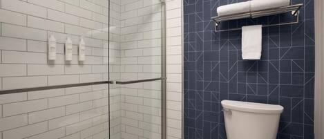 A bathroom with a glass shower enclosure, a white toilet, and a dark blue tiled wall.