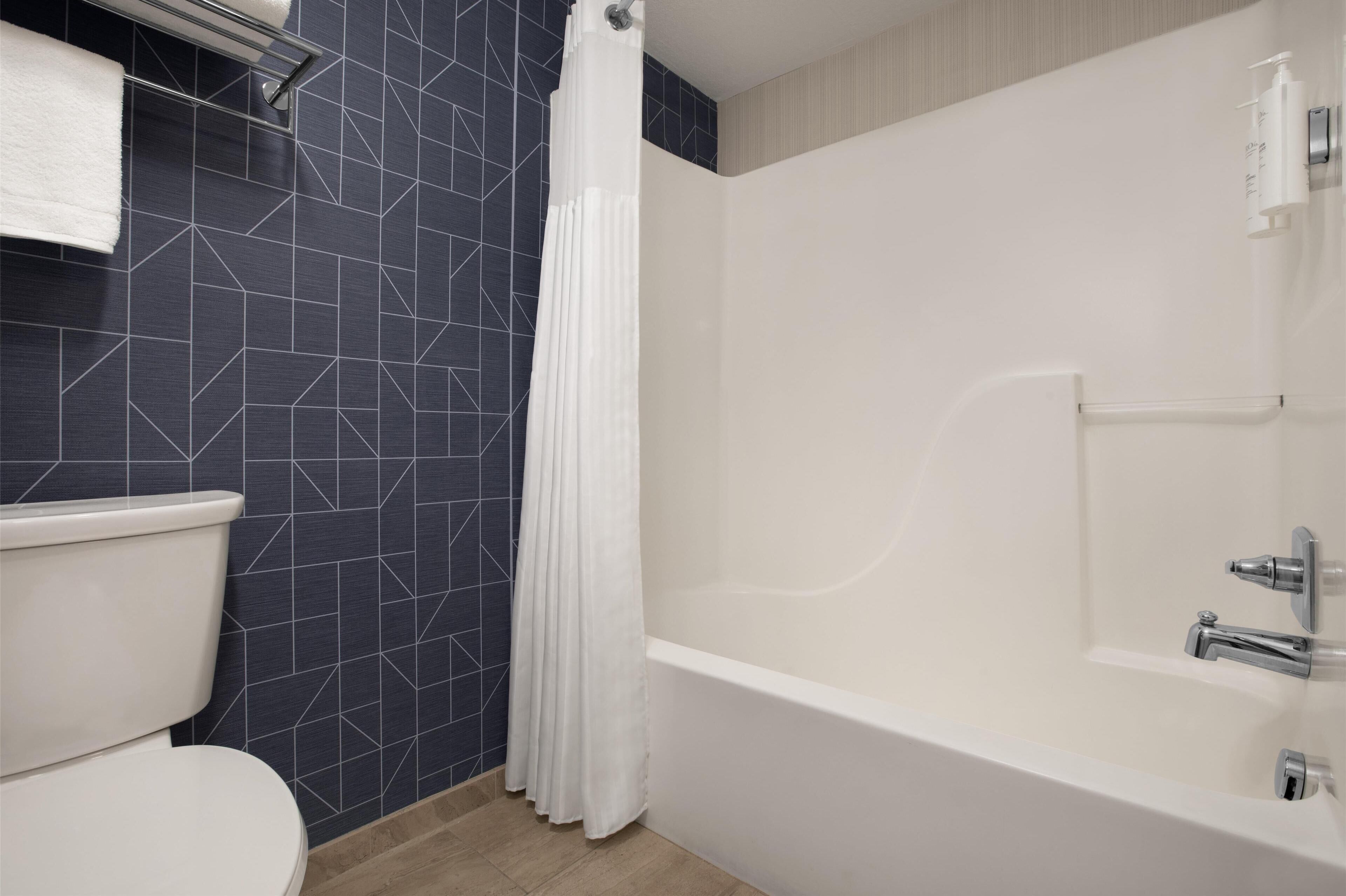 A modern bathroom with a white toilet, a bathtub with a shower curtain, and a wall with a geometric tile pattern.