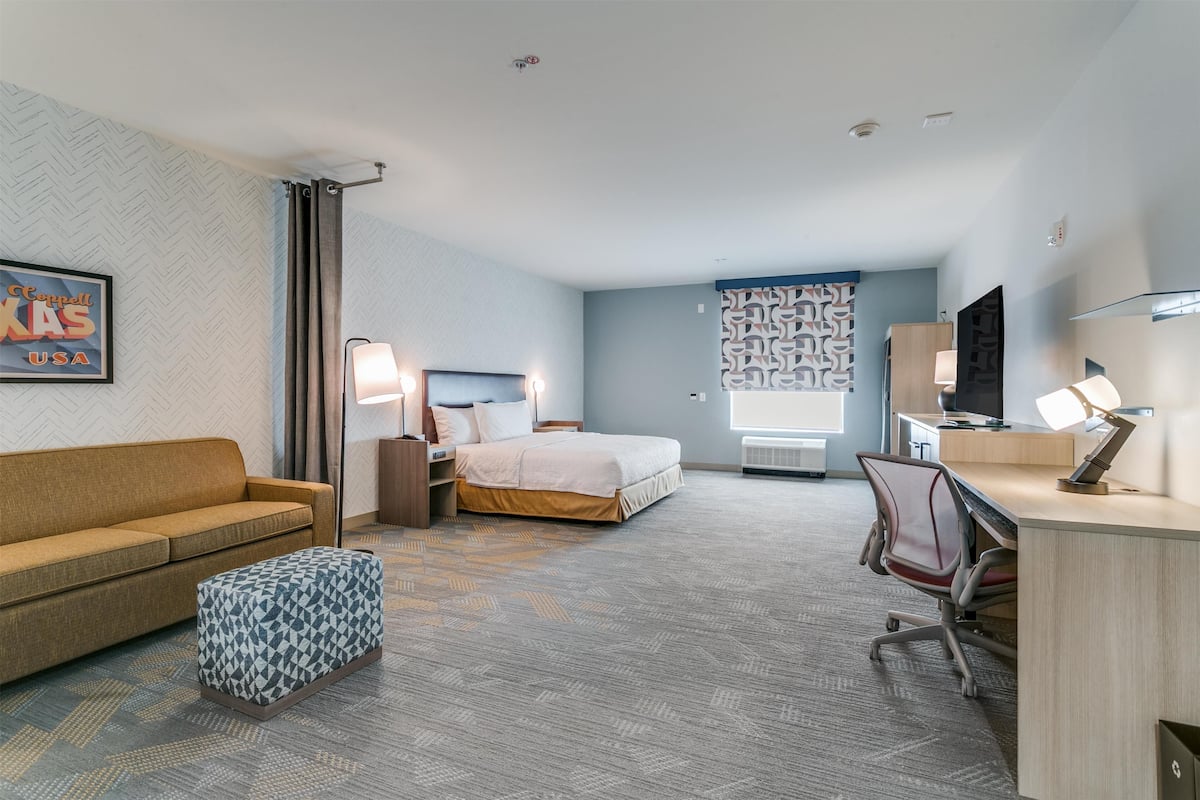 Una habitación de hotel con una cama, un escritorio, una silla, un sofá y un reposapiés estampado.