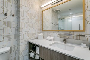 Un baño moderno con un revestimiento mural de diseño geométrico, un espejo grande, un lavabo y un inodoro.