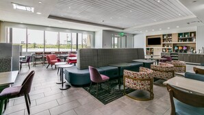 A modern indoor space with a seating area, tables, and a kitchen area with a TV.