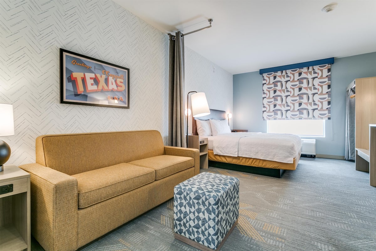 Habitación de hotel con sofá, cama, mesita de noche, lámpara y pared con estampado.
