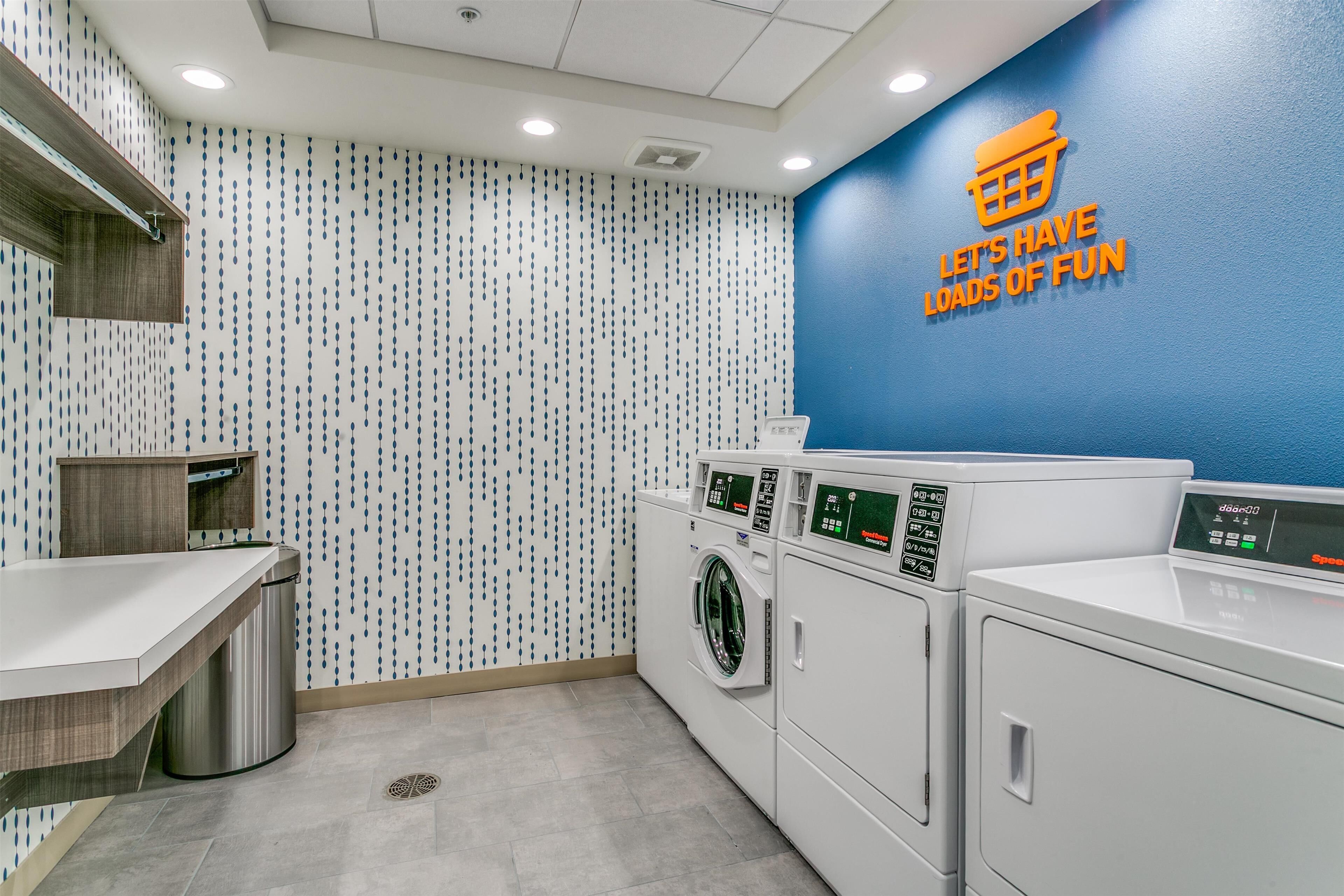 A laundry room with a blue wall, a wall-mounted sign, and a row of washing machines.