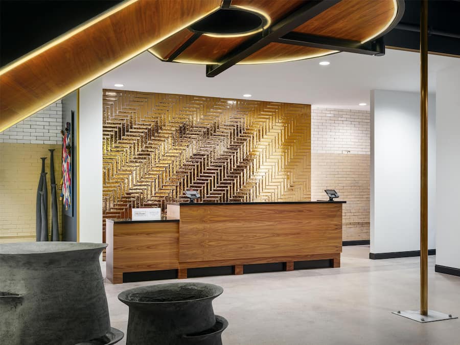 A modern hotel reception area with a wooden reception desk, a patterned wall, and a concrete planter.