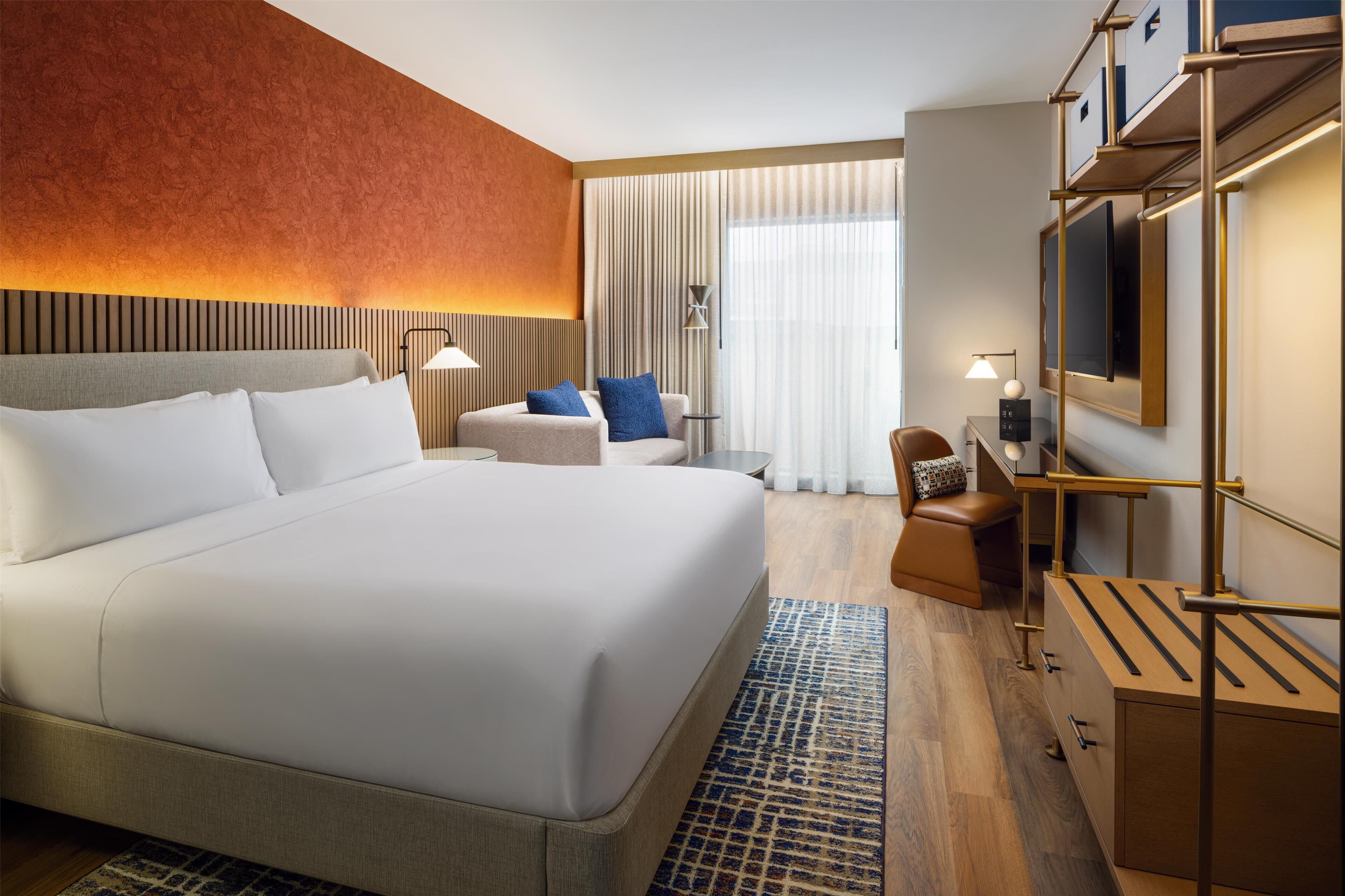 A modern hotel room with a large bed, a desk, a chair, and a television.