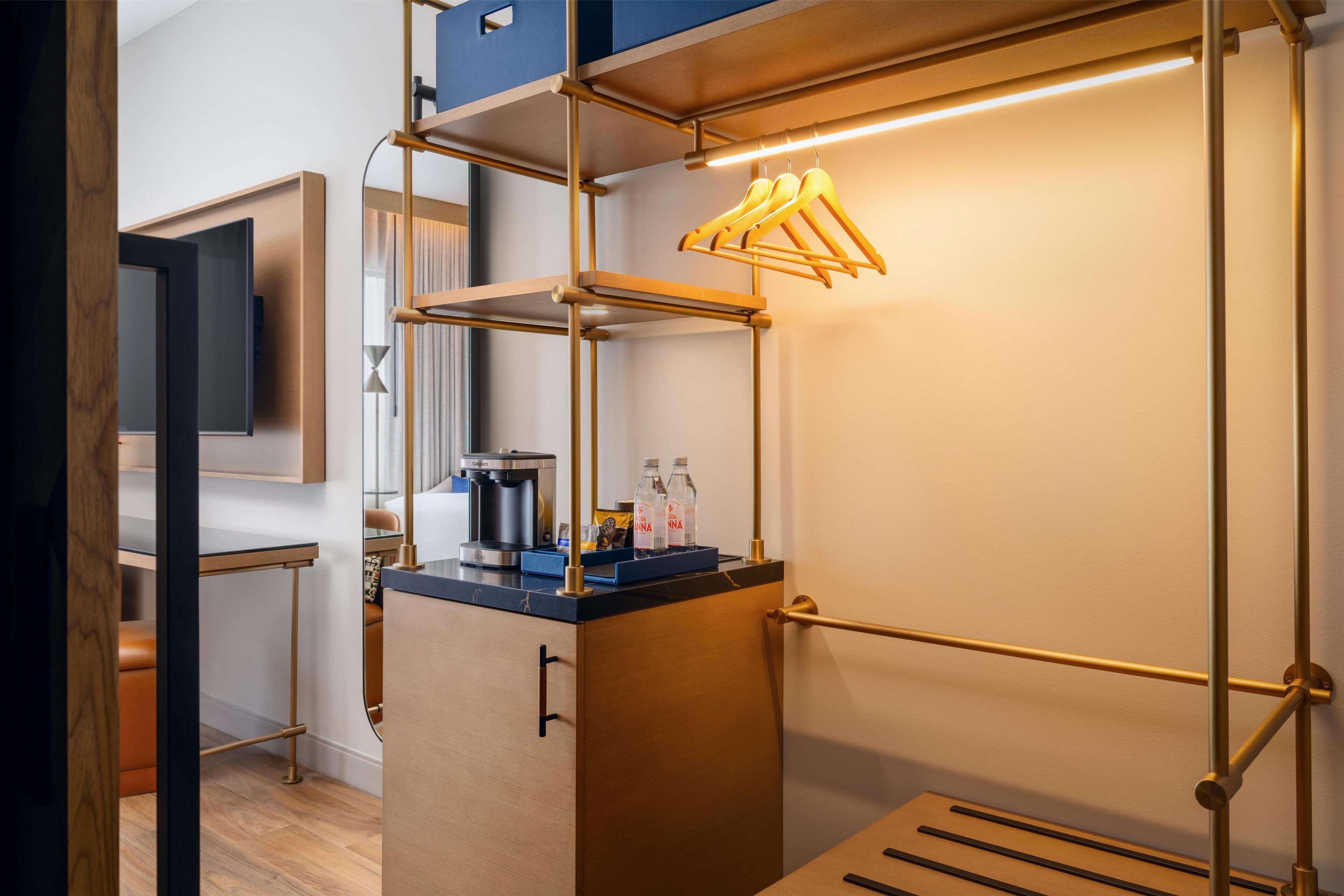 Ein modernes Hotelzimmer mit einem Holztisch, einer Kaffeemaschine und einem Regal mit Flaschen.