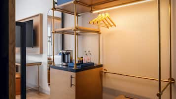 Habitació d'hotel moderna amb una taula de treball de fusta, una màquina de cafè i una estant amb ampolles.