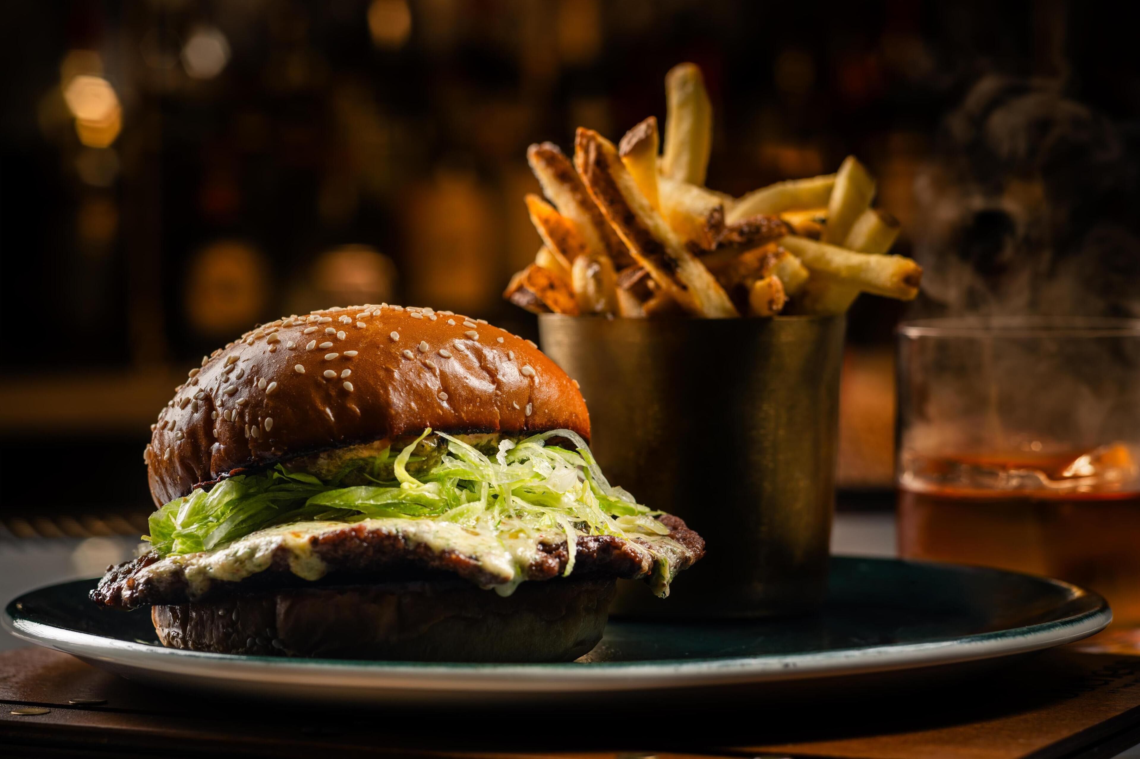 Un hamburger accompagné de frites et d’une boisson, le tout servi sur une assiette.