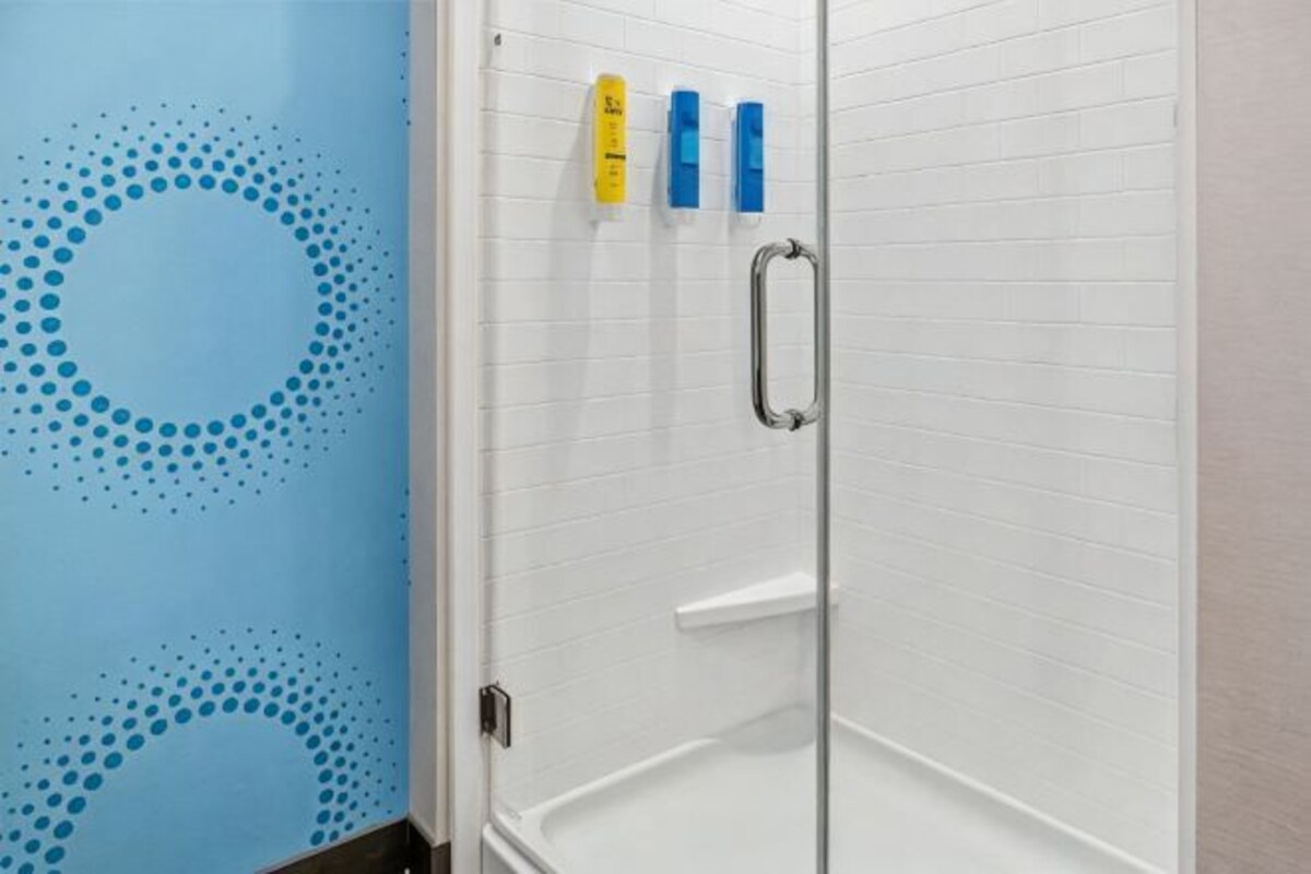 Een douche met een glazen deur, een witte betegelde muur en een blauwe muur met een cirkelpatroon.