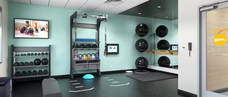 Ein modernes Fitnessstudio mit Trainingsgeräten, einem Wand-Fernseher und einem Spiegel.