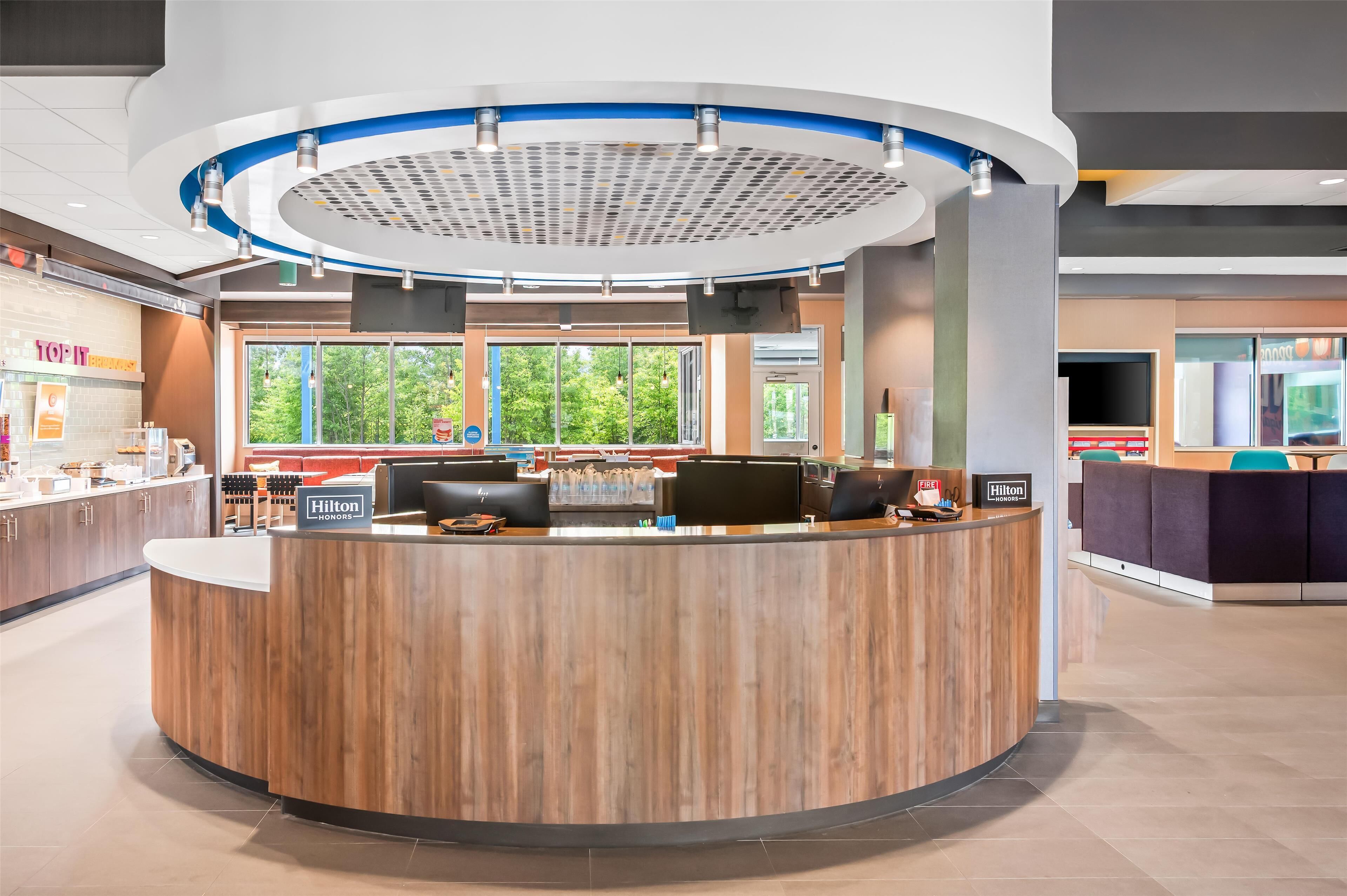 A hotel reception desk with a modern design, a large window offering a view of trees, and a sign indicating 'Hilton Honors'.