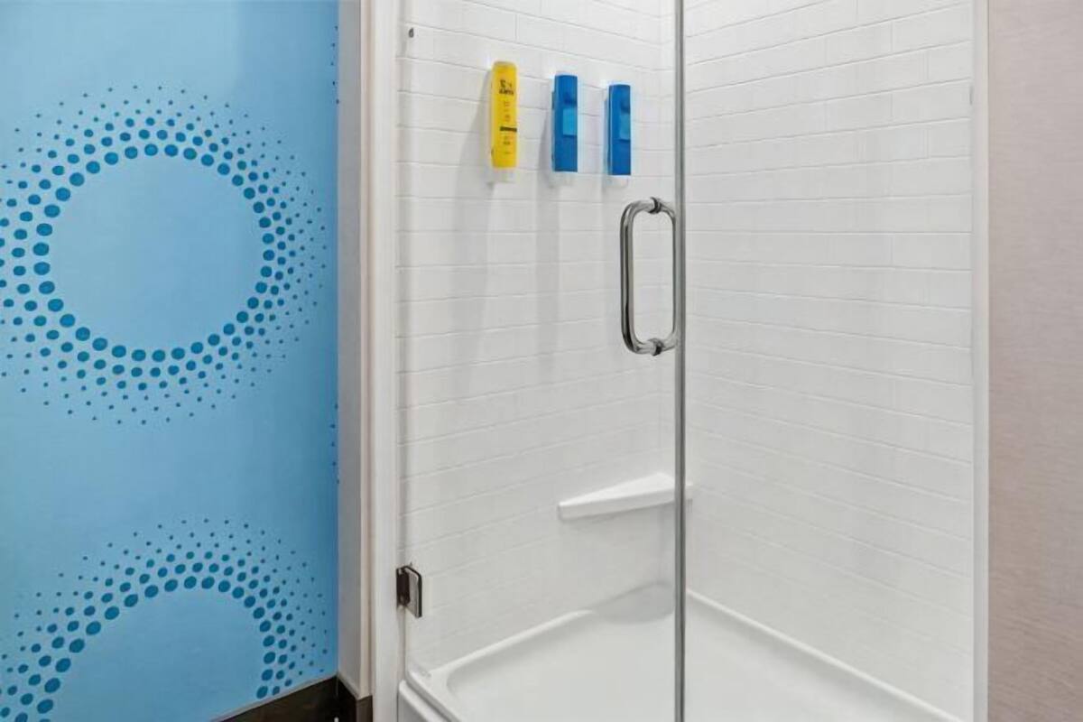 A shower with a glass door, a white tiled wall, and a blue wall with a circular pattern.