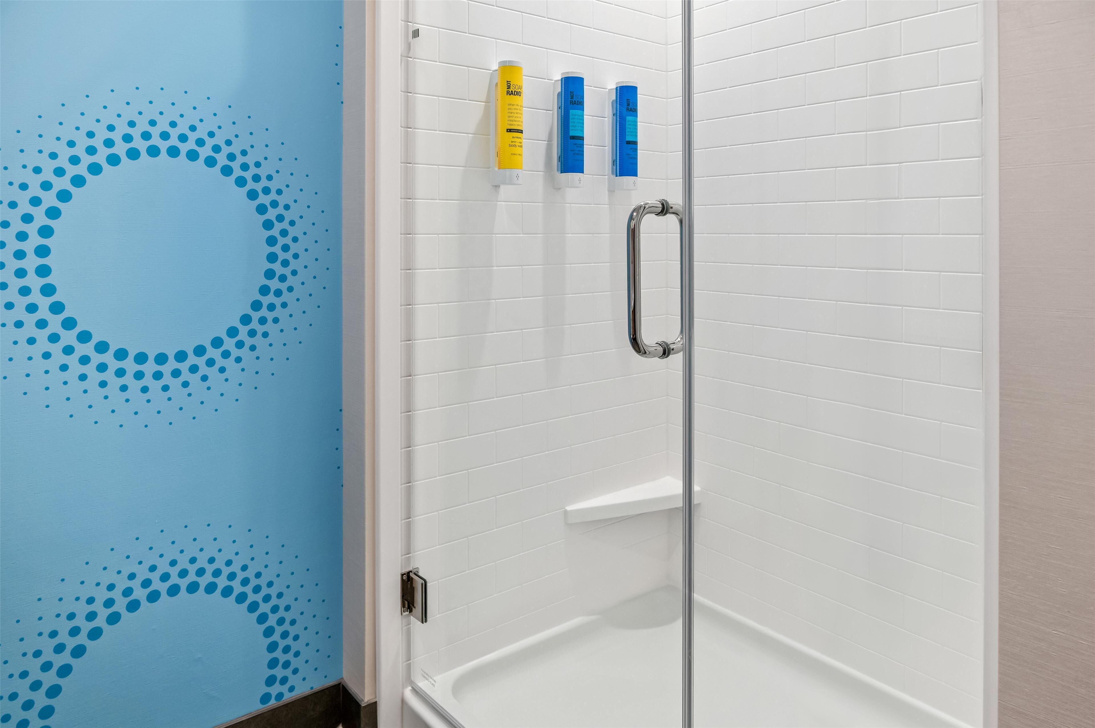 A shower area with white tiled walls, a glass door, and three toiletries on the wall.