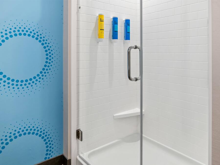 A shower area with white tiled walls, a glass door, and three toiletries on the wall.