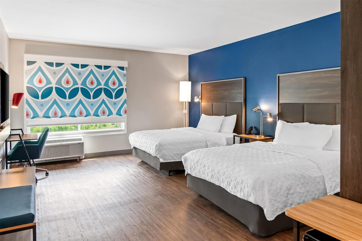 A hotel room with two beds, a desk, a chair, and a large window with a view.