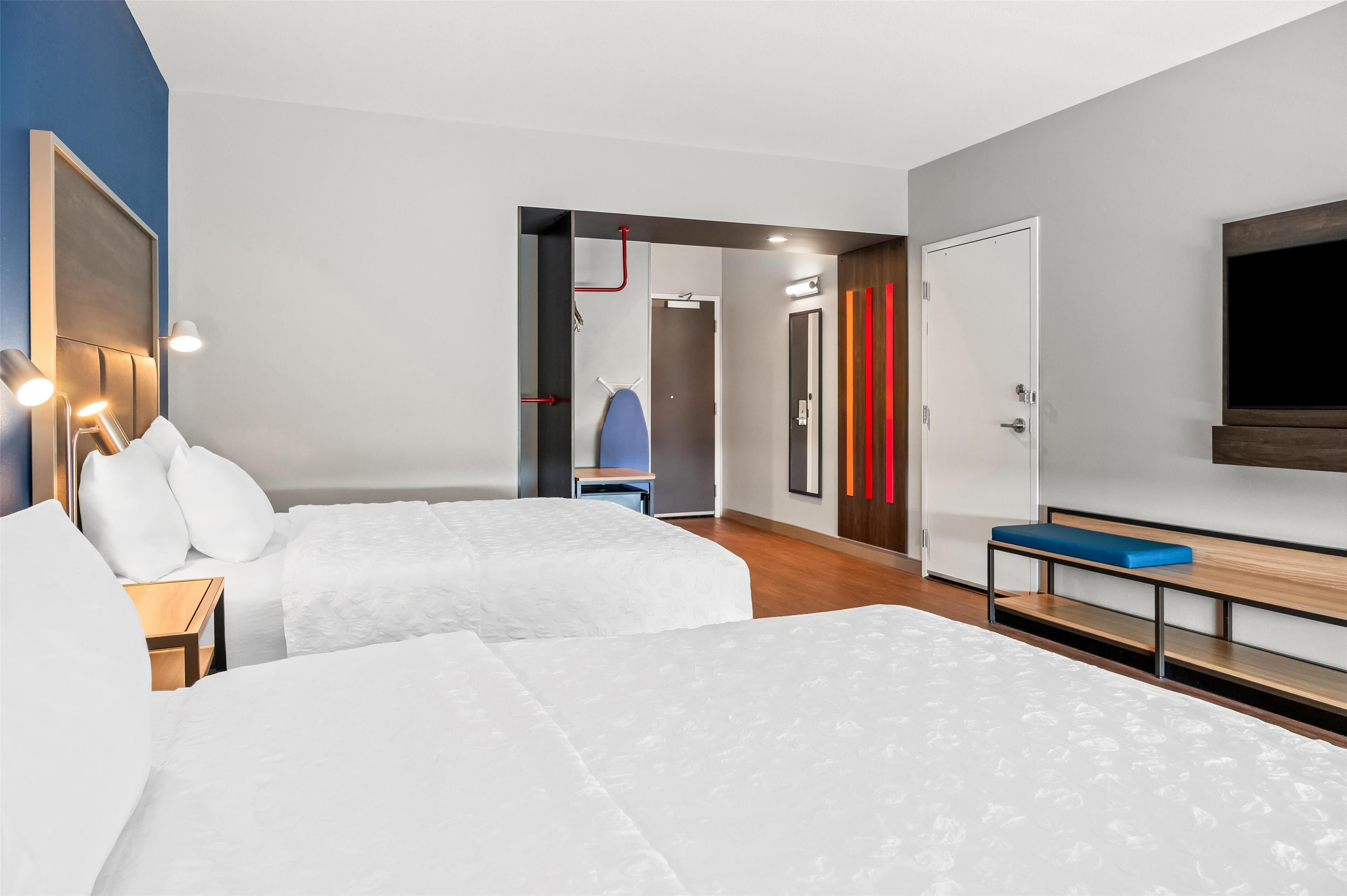 A hotel room with two beds, a desk, a chair, a TV, and a door.