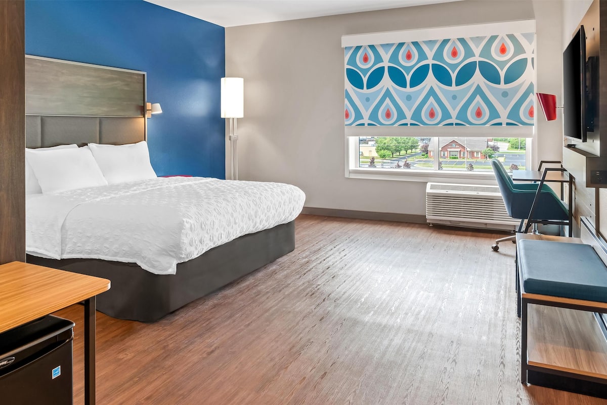 A hotel room with a bed, a desk, a chair, a TV, and a window with a view of the outside.