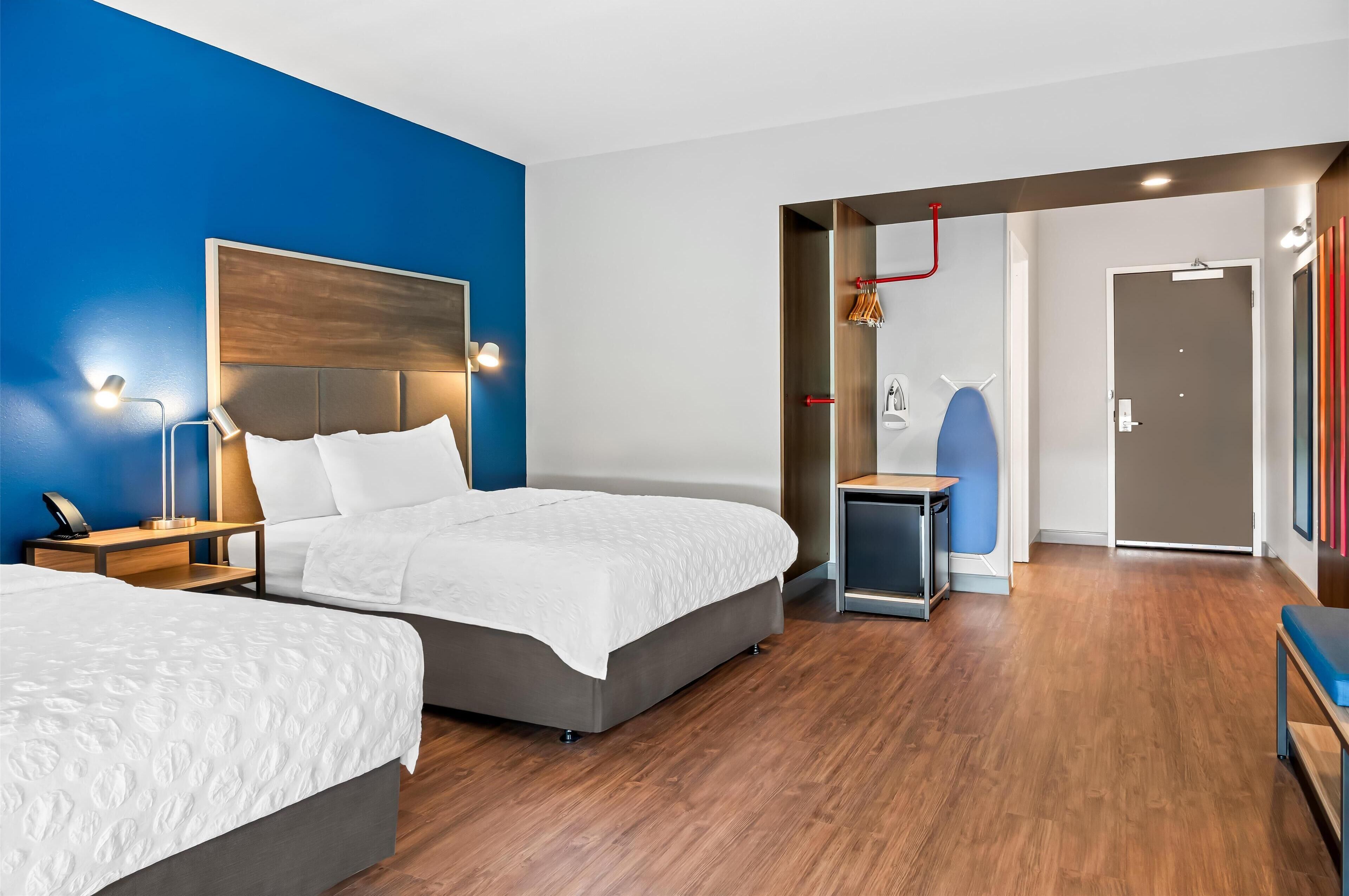 A modern hotel room with two beds, a desk, and a shower area.
