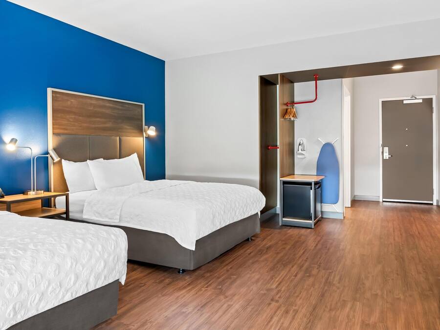 A modern hotel room with two beds, a desk, and a shower area.