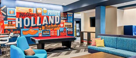 A lounge area with a pool table, blue sofas, and a colorful wall mural.