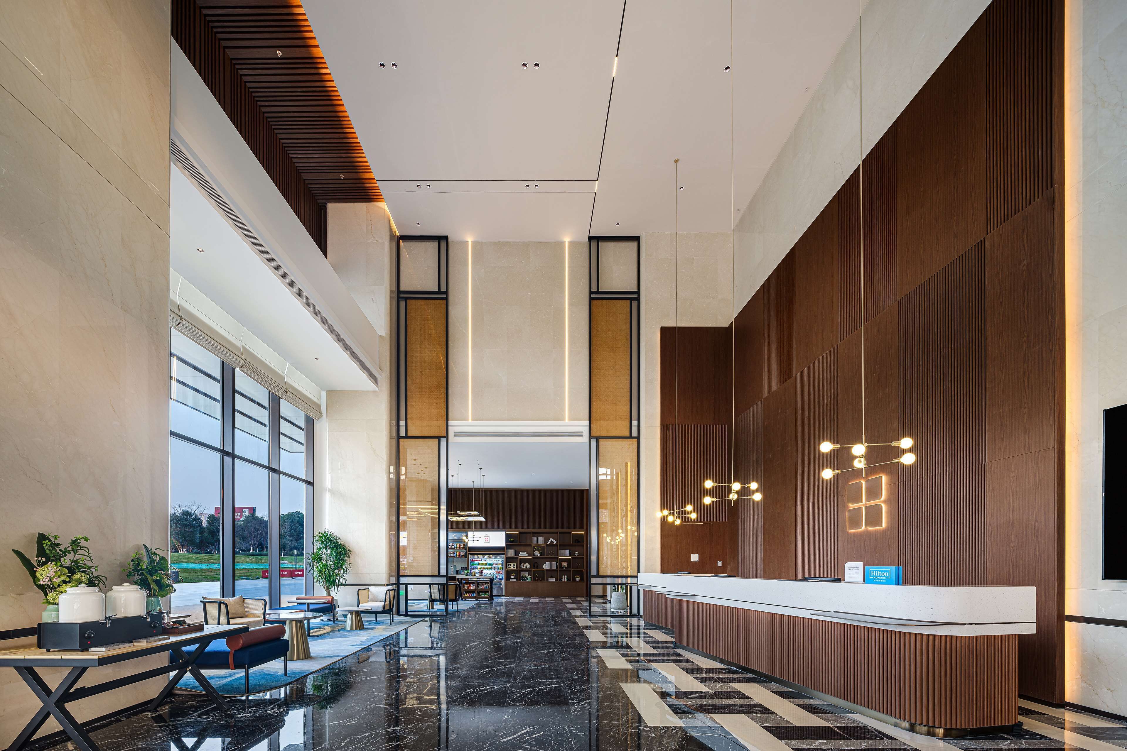 A modern hotel lobby with a reception desk, seating area, and large windows offering a view of the outdoors.