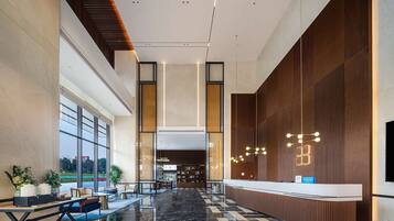 A modern hotel lobby with a reception desk, seating area, and large windows offering a view of the outdoors.