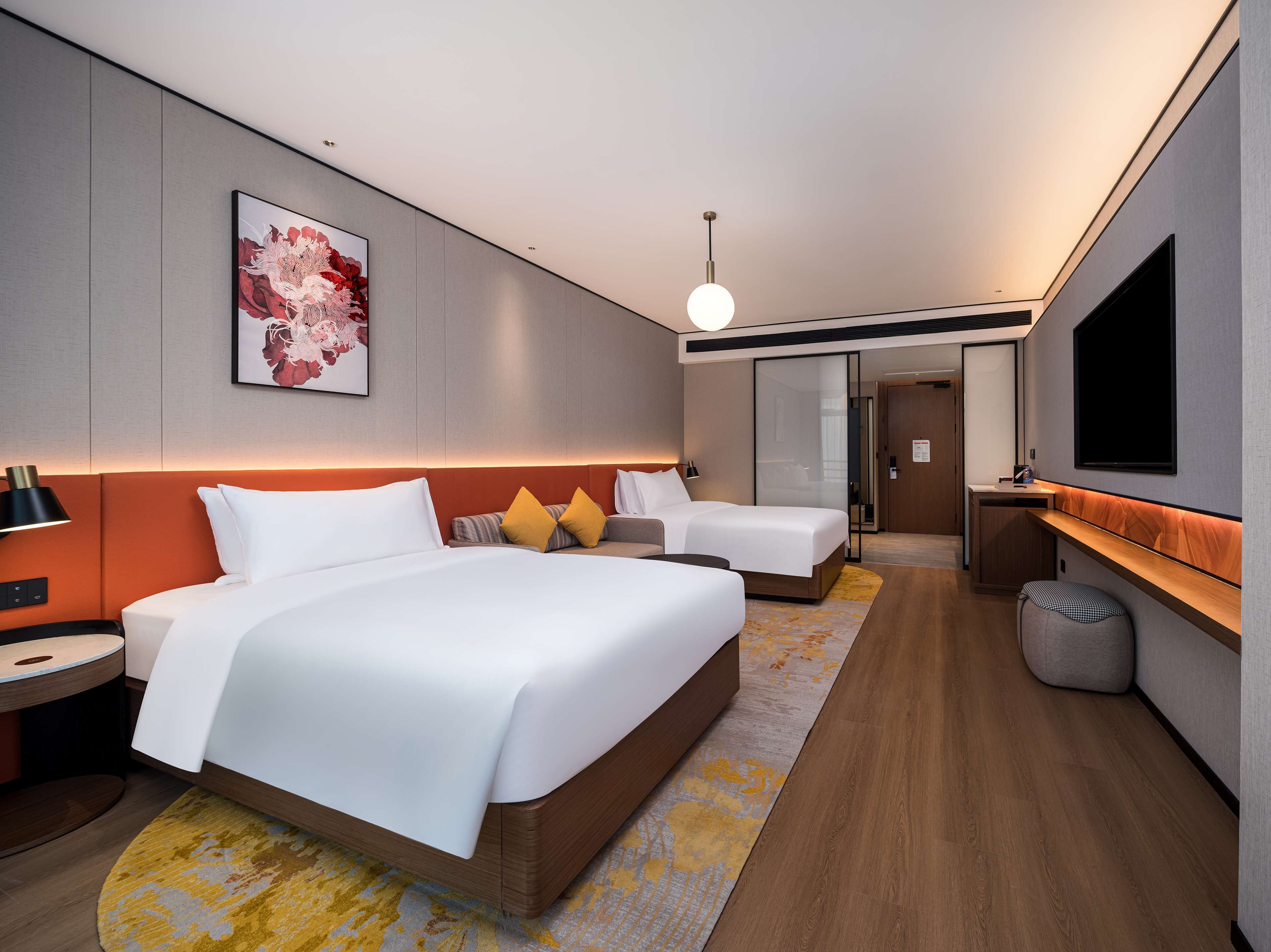 A modern hotel room with a large bed, a smaller bed, a desk, a TV, and a bathroom.
