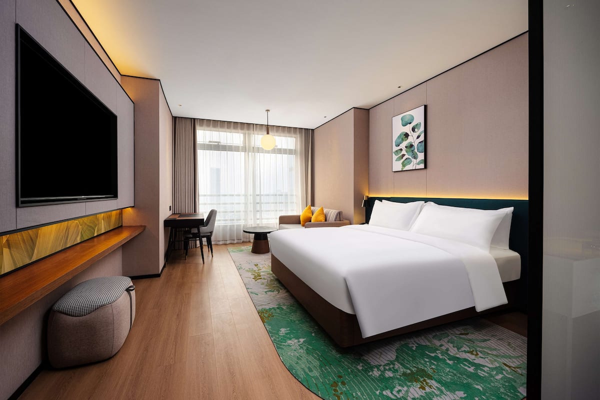 A modern hotel room with a large bed, a desk, and a TV.