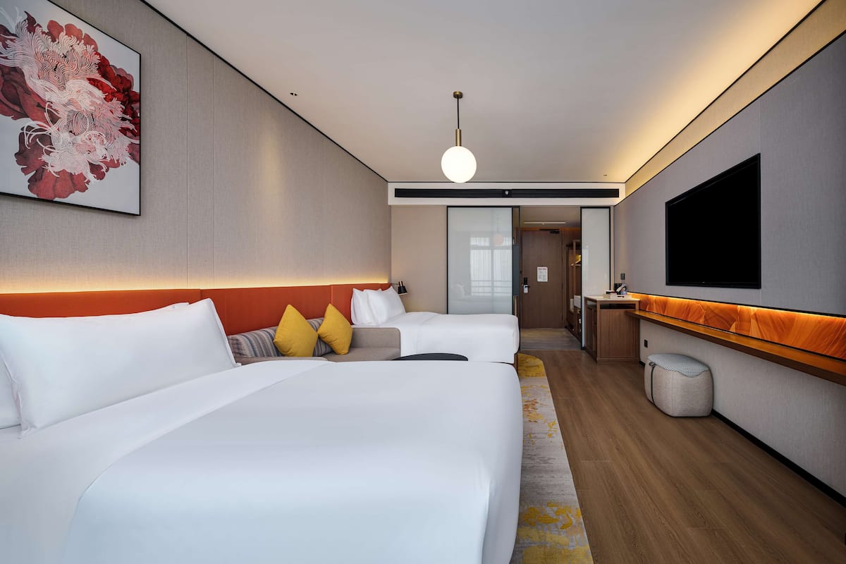 A hotel room with two beds, a TV, a painting, and a wooden floor.