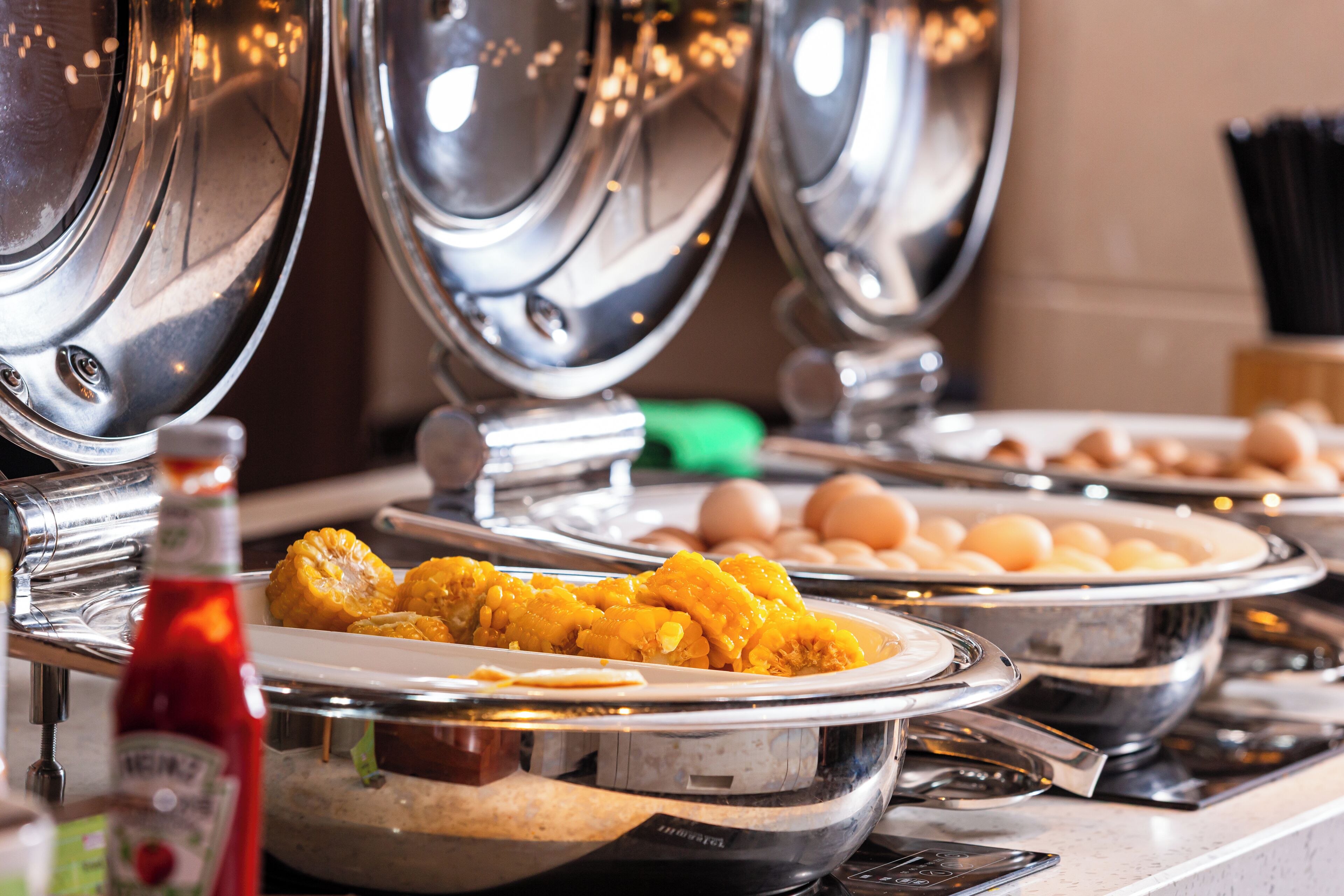 A buffet setup with various dishes and a bottle of ketchup.