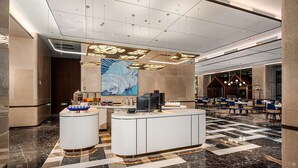 Un hall d’hôtel moderne avec un comptoir d’accueil, une grande peinture abstraite et un espace repas comprenant des tables et des chaises.