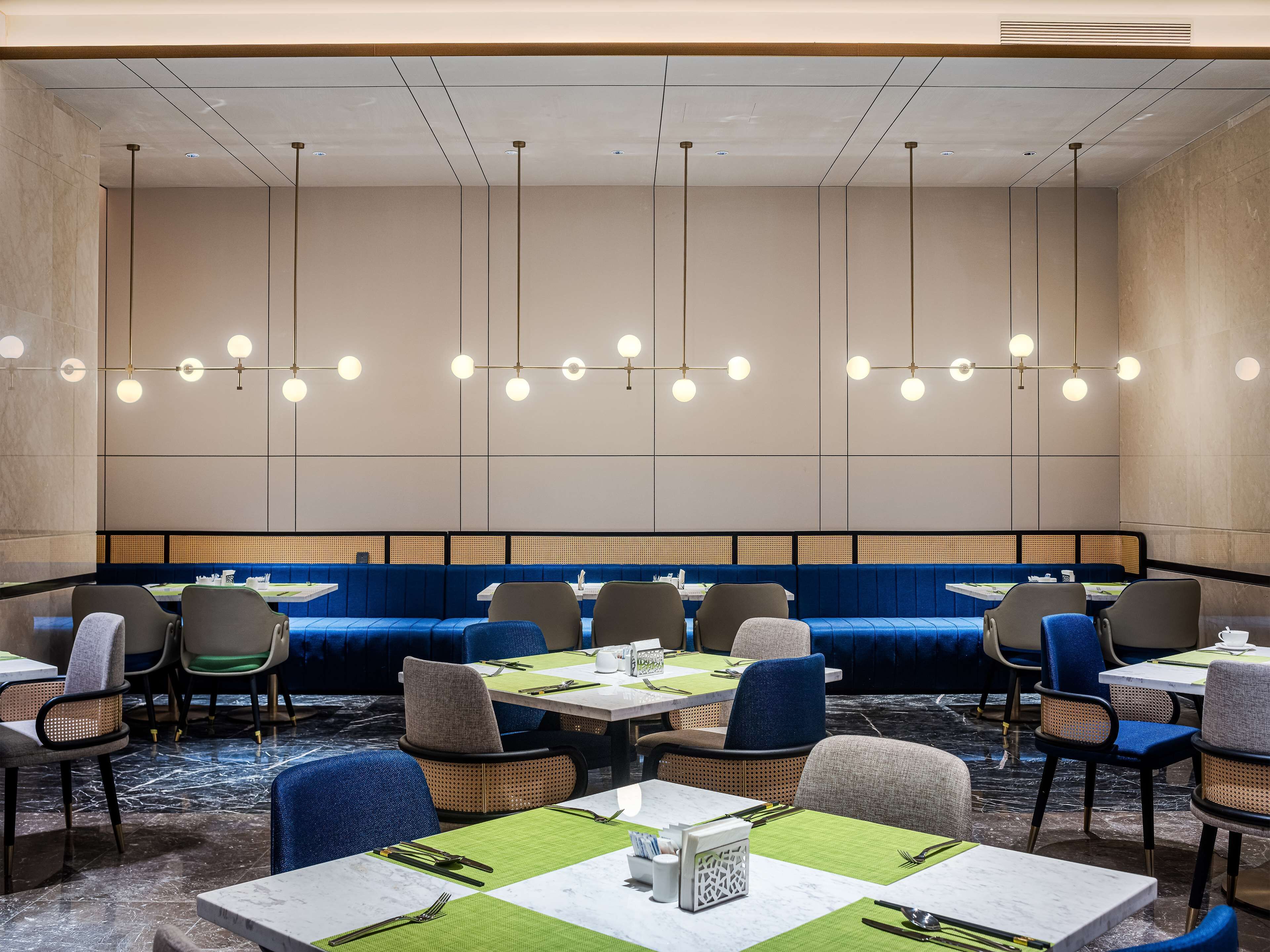 A modern restaurant with a long blue booth seating area, individual tables with chairs, and pendant lighting.