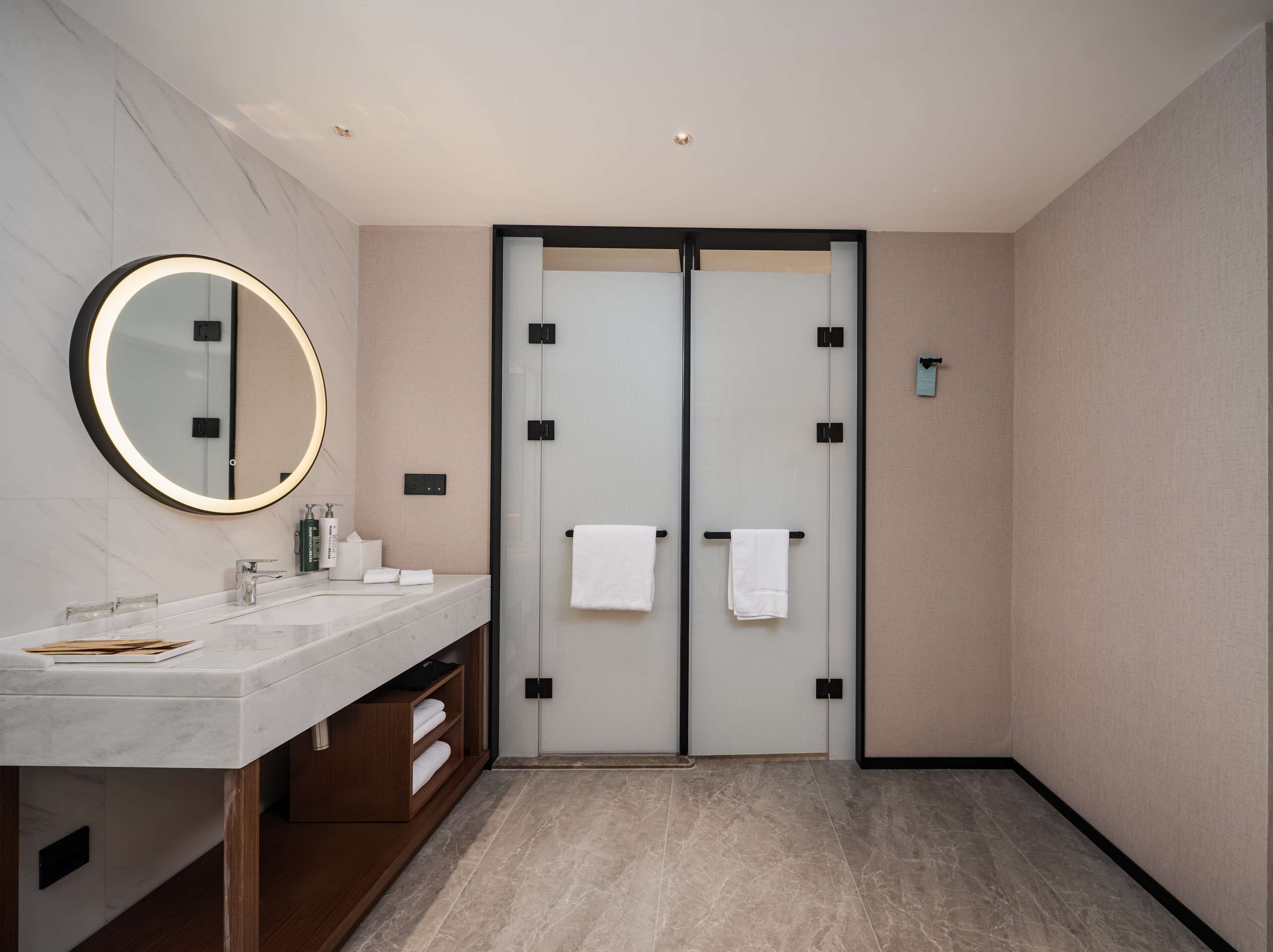 A modern bathroom with a marble vanity, a large mirror, and a double door with towels.
