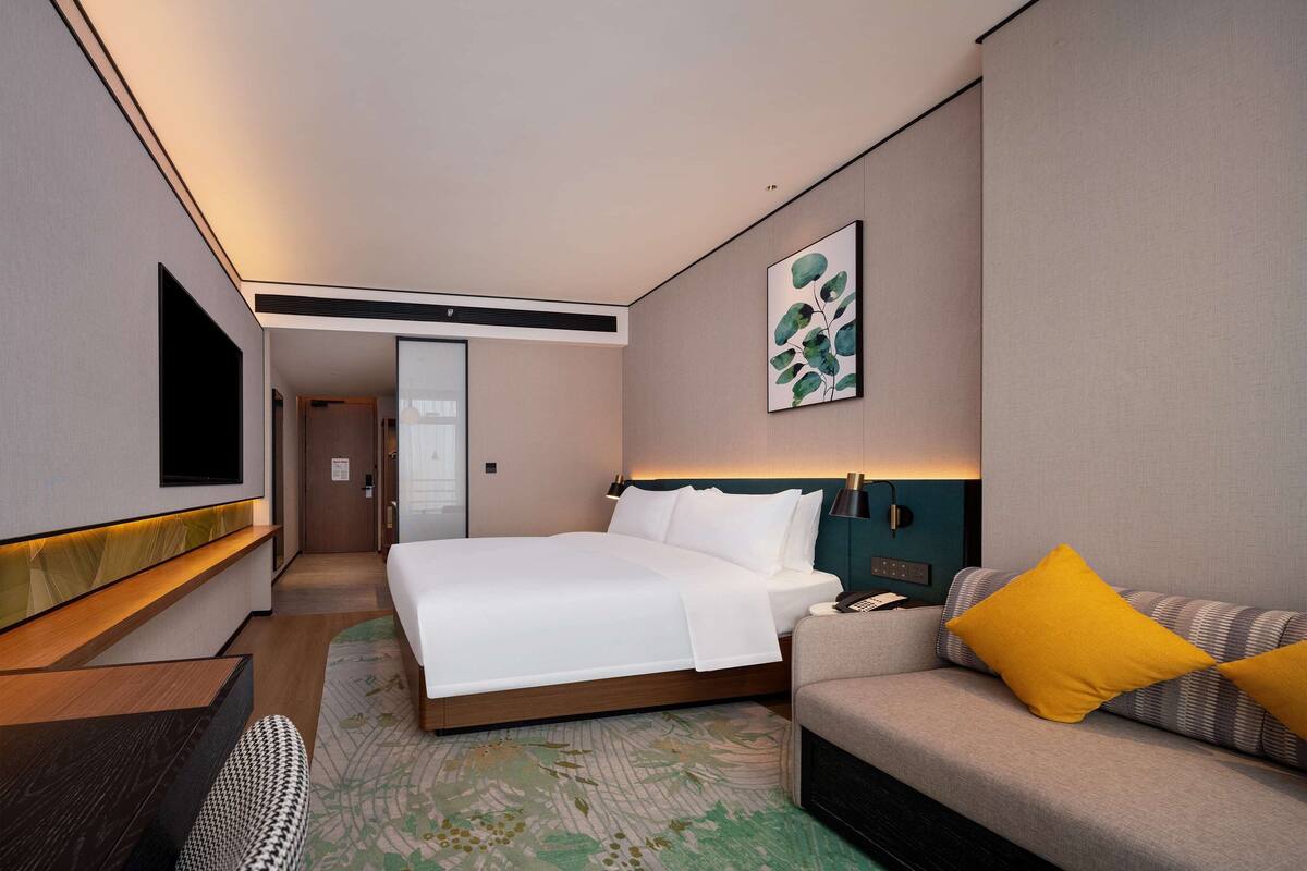 A hotel room with a bed, a sofa, a TV, and a painting on the wall.