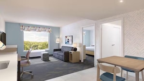 A hotel room with a large window, a sofa, a desk, and a dining table. - Home2 Suites By Hilton Woodland Sacramento (Woodland)