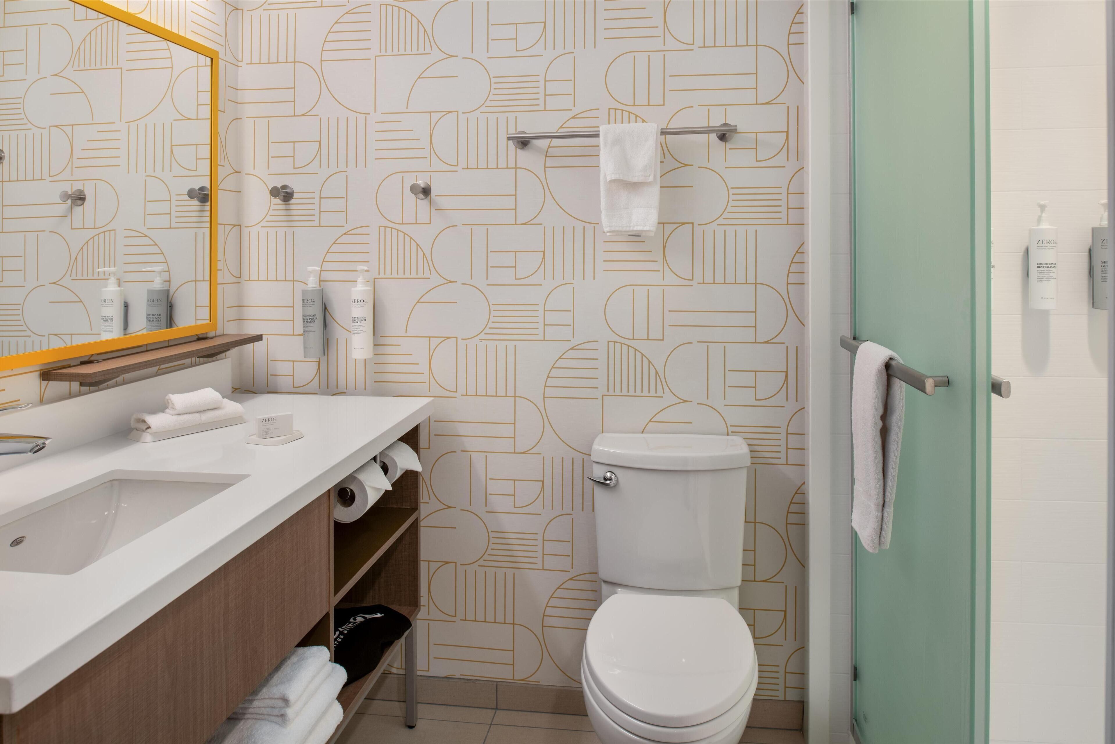 A modern bathroom with a geometric patterned wall, a white sink, a toilet, and a glass shower enclosure.