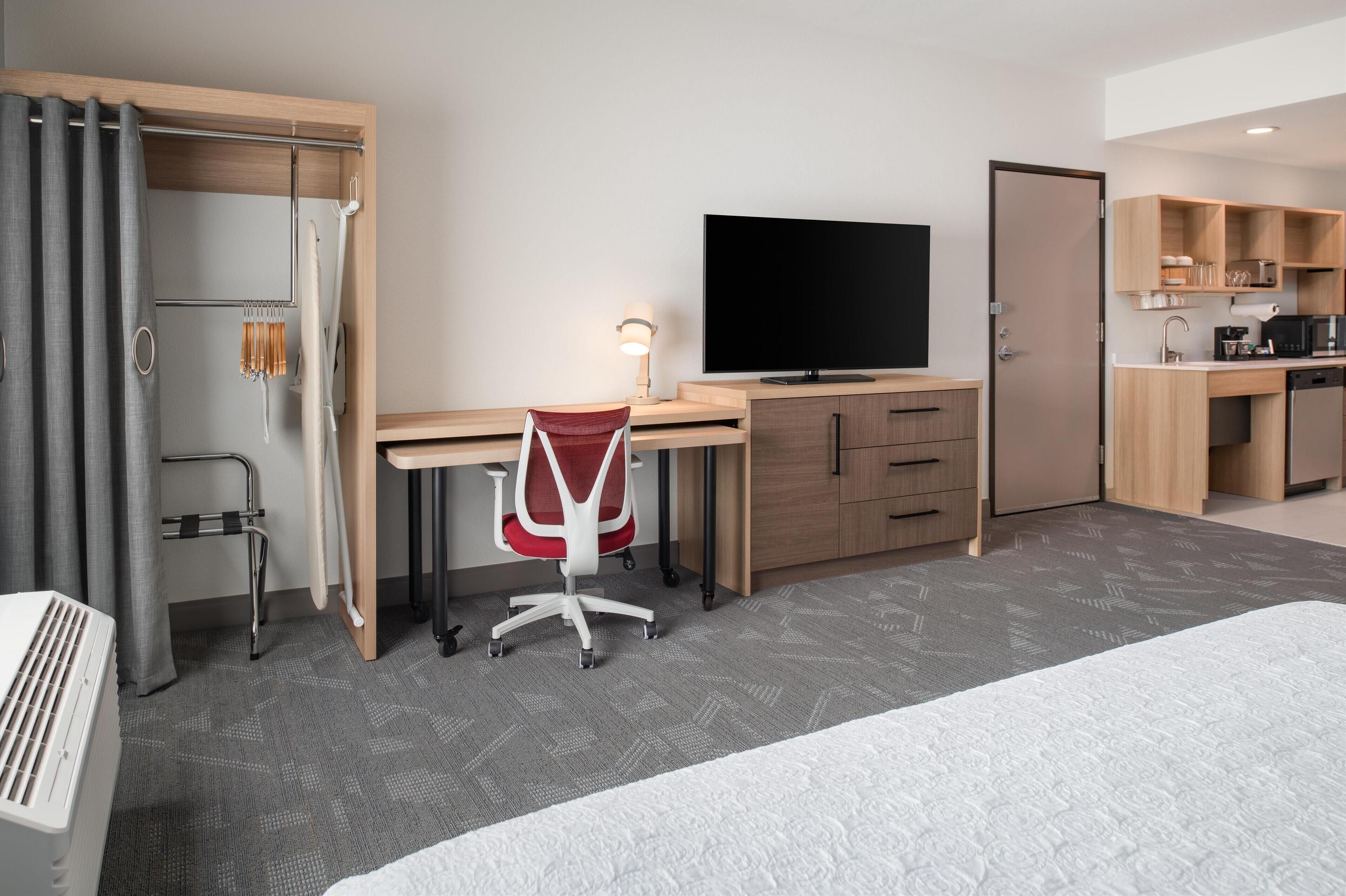 Habitación de hotel con cama, escritorio y silla, televisión, armario y kitchenette.