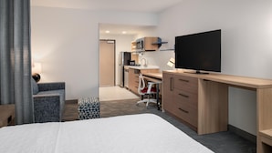 A hotel room with a bed, a desk, a TV, a kitchenette, and a chair. - Home2 Suites By Hilton Woodland Sacramento (Woodland)