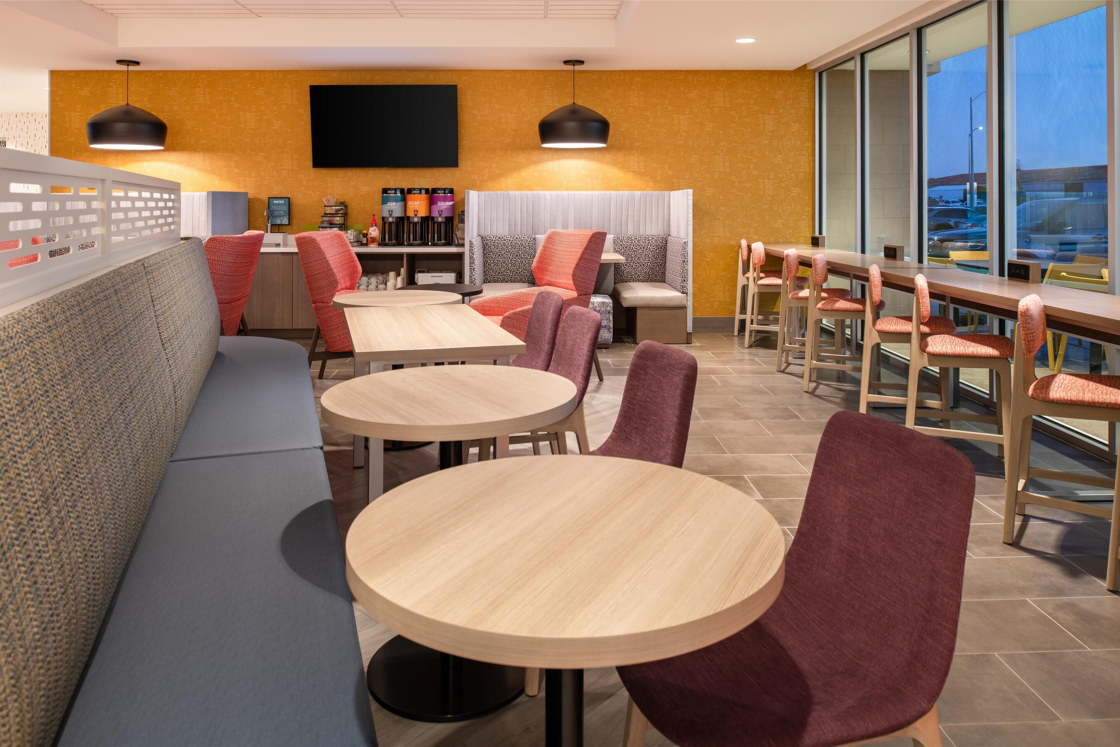 A modern restaurant with round tables and booths, a flat-screen TV, and a view of the cityscape.